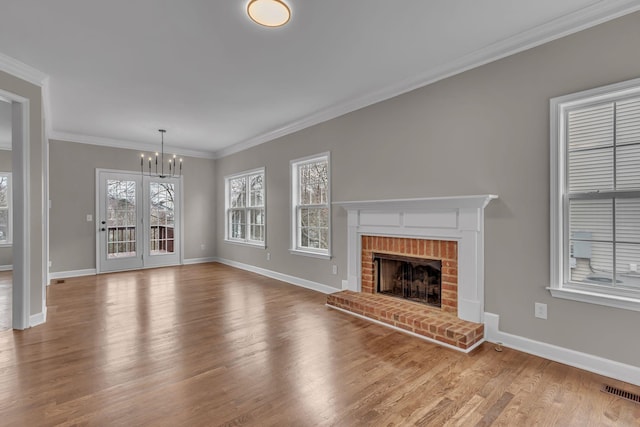 unfurnished living room featuring an inviting chandelier, light hardwood / wood-style floors, a brick fireplace, and crown molding