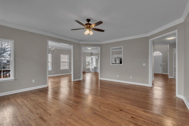 unfurnished living room with wood-type flooring, ceiling fan with notable chandelier, and ornamental molding