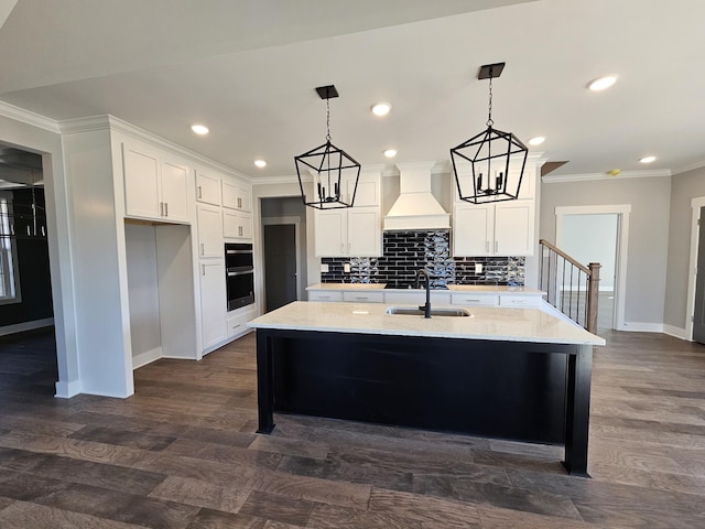 kitchen featuring a kitchen island with sink, custom range hood, sink, and white cabinets