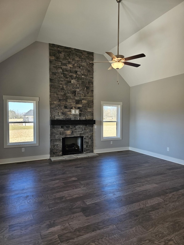 unfurnished living room with a healthy amount of sunlight, dark hardwood / wood-style floors, vaulted ceiling, and a stone fireplace