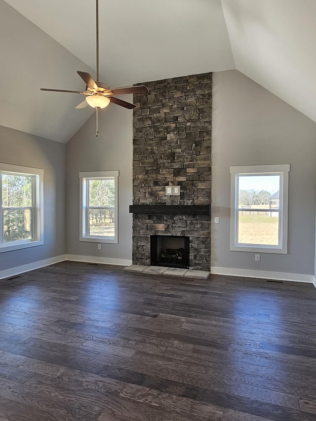 unfurnished living room featuring vaulted ceiling, a healthy amount of sunlight, a stone fireplace, and dark hardwood / wood-style floors