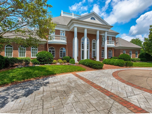 greek revival house featuring brick siding, a front lawn, and a balcony