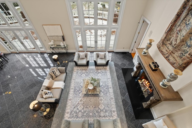 living area featuring french doors, granite finish floor, a towering ceiling, and baseboards