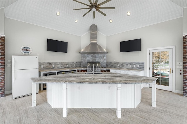 kitchen with freestanding refrigerator, vaulted ceiling, wall chimney range hood, and a breakfast bar area