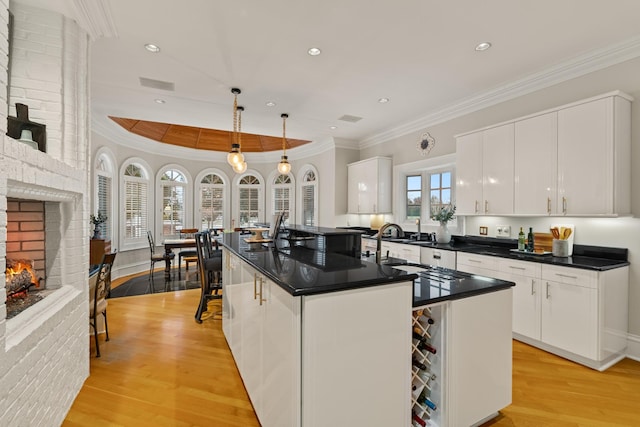 kitchen with light wood finished floors, white cabinets, dark countertops, crown molding, and a brick fireplace