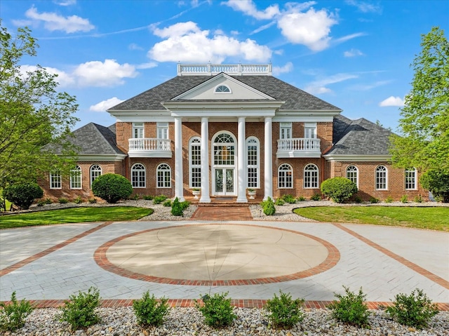 exterior space featuring brick siding, curved driveway, french doors, and a balcony
