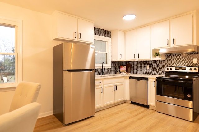 kitchen with appliances with stainless steel finishes, tasteful backsplash, sink, white cabinets, and light hardwood / wood-style flooring