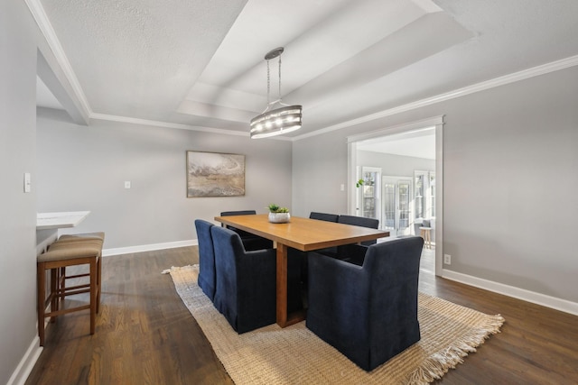 dining area with ornamental molding, a textured ceiling, a raised ceiling, and dark wood-type flooring