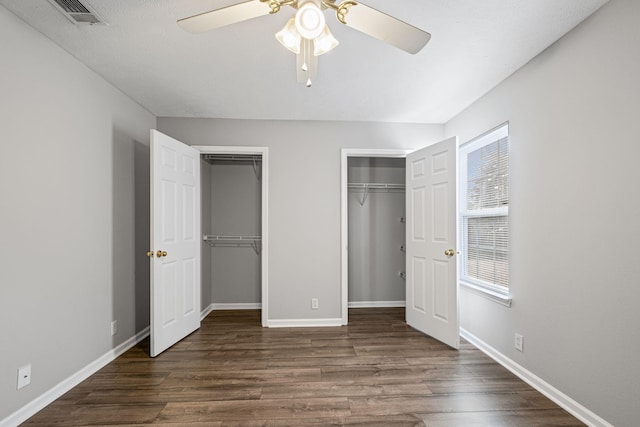 unfurnished bedroom with dark hardwood / wood-style flooring, two closets, and ceiling fan