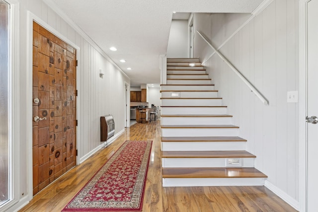 staircase featuring a textured ceiling, hardwood / wood-style flooring, and heating unit