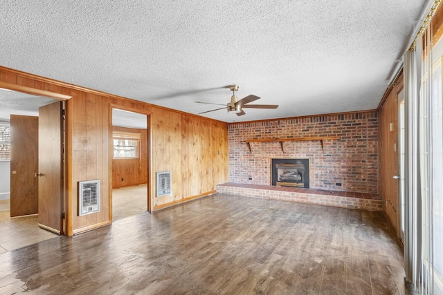 unfurnished living room featuring hardwood / wood-style flooring, a textured ceiling, wooden walls, and heating unit