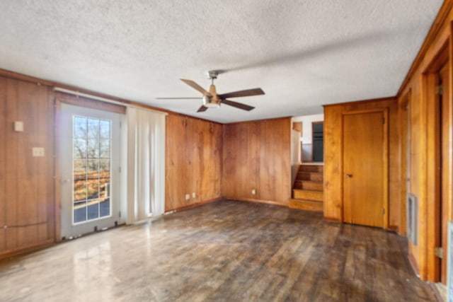 interior space featuring a textured ceiling, wooden walls, ceiling fan, and dark hardwood / wood-style floors