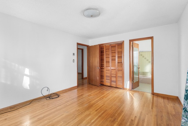 unfurnished bedroom featuring a closet, light wood-type flooring, and ensuite bath