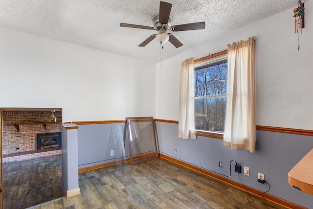 empty room with ceiling fan, dark wood-type flooring, a textured ceiling, and a brick fireplace