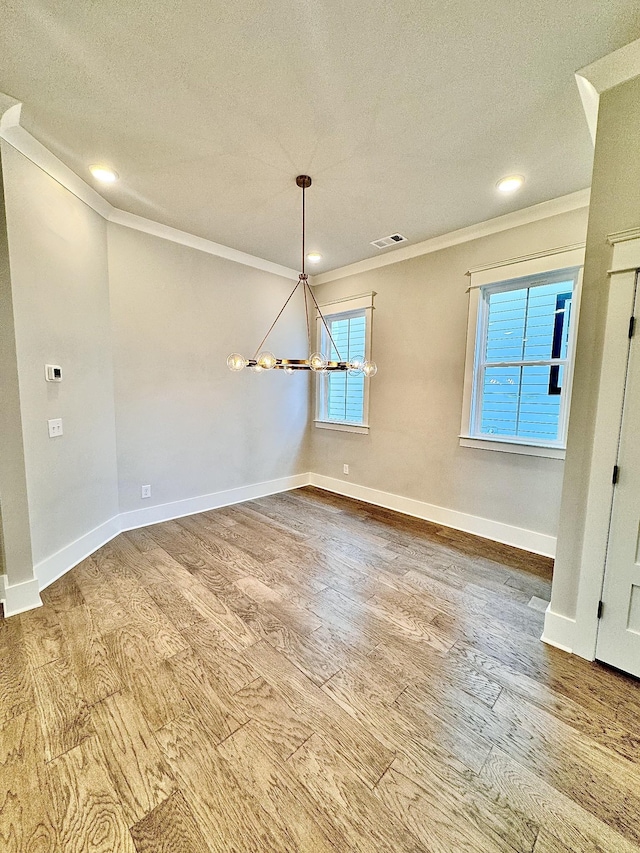 unfurnished dining area with hardwood / wood-style flooring, a textured ceiling, ornamental molding, and a chandelier