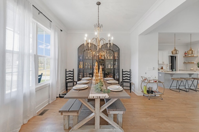 dining area featuring ornamental molding, light hardwood / wood-style floors, and a notable chandelier