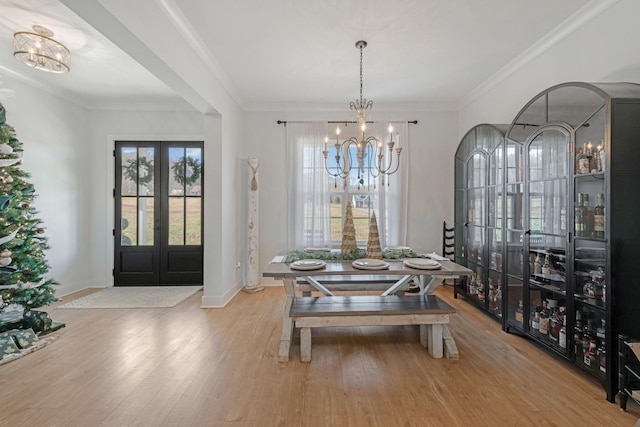 dining room featuring french doors, light hardwood / wood-style floors, an inviting chandelier, and ornamental molding