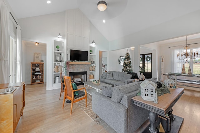 living room with a fireplace, high vaulted ceiling, ceiling fan with notable chandelier, and light wood-type flooring