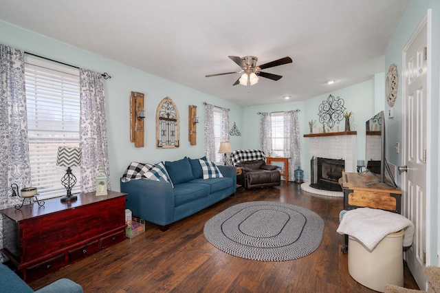 living room with dark wood-type flooring, ceiling fan, and a brick fireplace