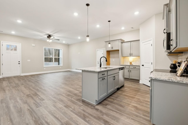 kitchen with sink, stainless steel dishwasher, an island with sink, pendant lighting, and light hardwood / wood-style floors