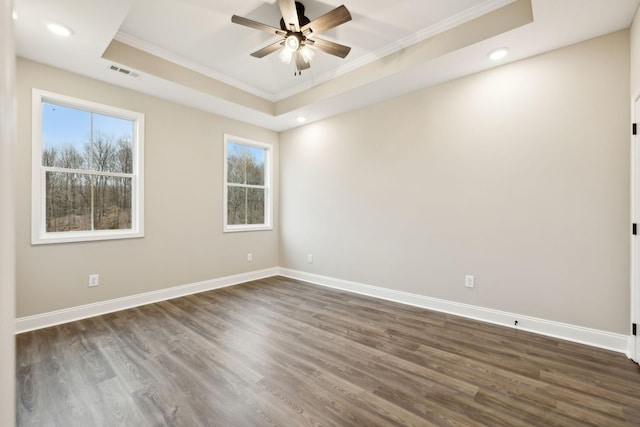 empty room featuring dark hardwood / wood-style flooring, a tray ceiling, ceiling fan, and ornamental molding