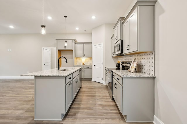 kitchen featuring sink, pendant lighting, a kitchen island with sink, appliances with stainless steel finishes, and light wood-type flooring