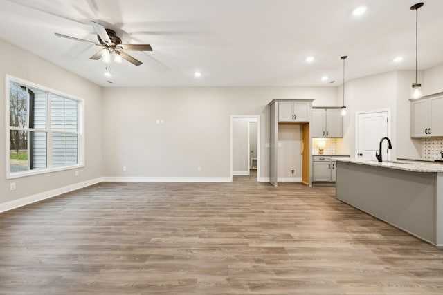 kitchen with ceiling fan, tasteful backsplash, light stone counters, light hardwood / wood-style flooring, and decorative light fixtures