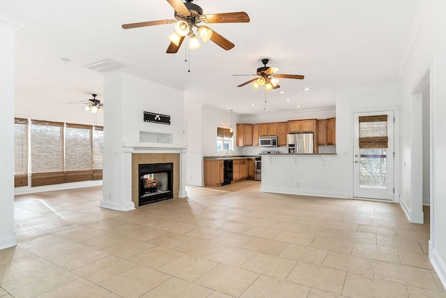 unfurnished living room with a tile fireplace, sink, ceiling fan, light tile patterned floors, and ornamental molding