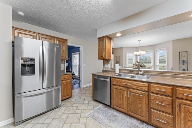 kitchen with appliances with stainless steel finishes, pendant lighting, sink, a notable chandelier, and a textured ceiling