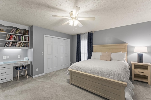 carpeted bedroom with built in desk, a textured ceiling, ceiling fan, and a closet