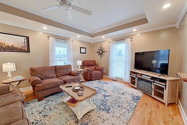 living room featuring a tray ceiling, plenty of natural light, ornamental molding, and light wood-type flooring