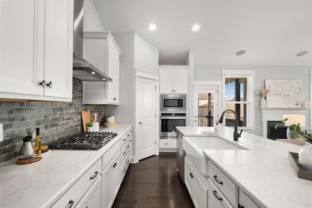 kitchen with appliances with stainless steel finishes, dark hardwood / wood-style flooring, sink, wall chimney range hood, and white cabinets