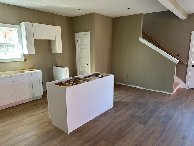 kitchen with wood finished floors, a kitchen island, beam ceiling, and white cabinets