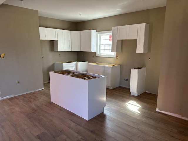 kitchen featuring white cabinets, a center island, baseboards, and wood finished floors