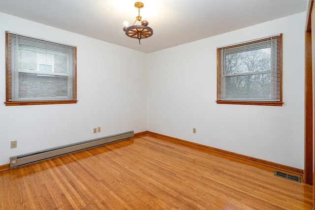 unfurnished room with hardwood / wood-style flooring, baseboard heating, a wealth of natural light, and a chandelier