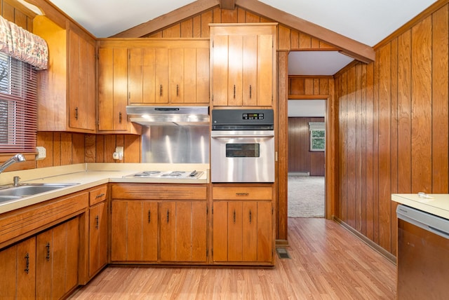 kitchen featuring lofted ceiling, sink, wooden walls, light wood-type flooring, and appliances with stainless steel finishes