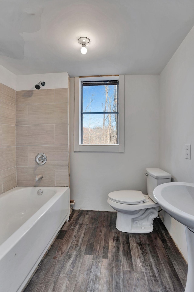 bathroom with wood-type flooring, toilet, and tiled shower / bath