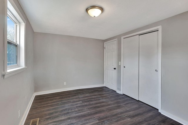 unfurnished bedroom featuring a textured ceiling, a closet, dark hardwood / wood-style floors, and multiple windows