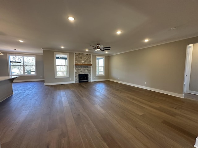 unfurnished living room featuring ceiling fan, a stone fireplace, ornamental molding, and dark hardwood / wood-style floors