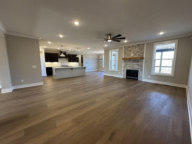 unfurnished living room with ceiling fan, dark wood-type flooring, ornamental molding, and a fireplace