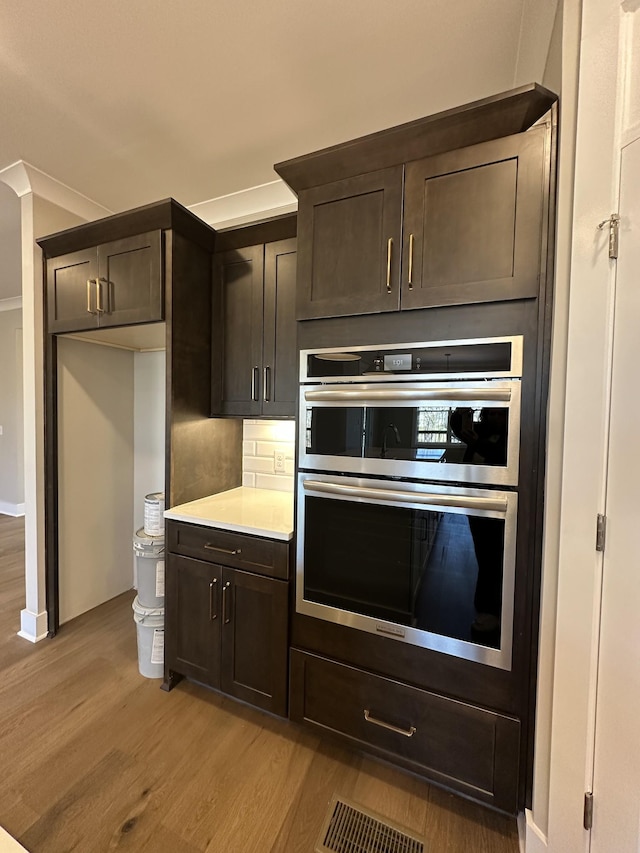 kitchen featuring double oven, ornamental molding, light hardwood / wood-style floors, and dark brown cabinetry