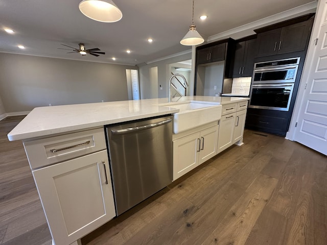 kitchen with light stone counters, stainless steel appliances, an island with sink, white cabinets, and ceiling fan