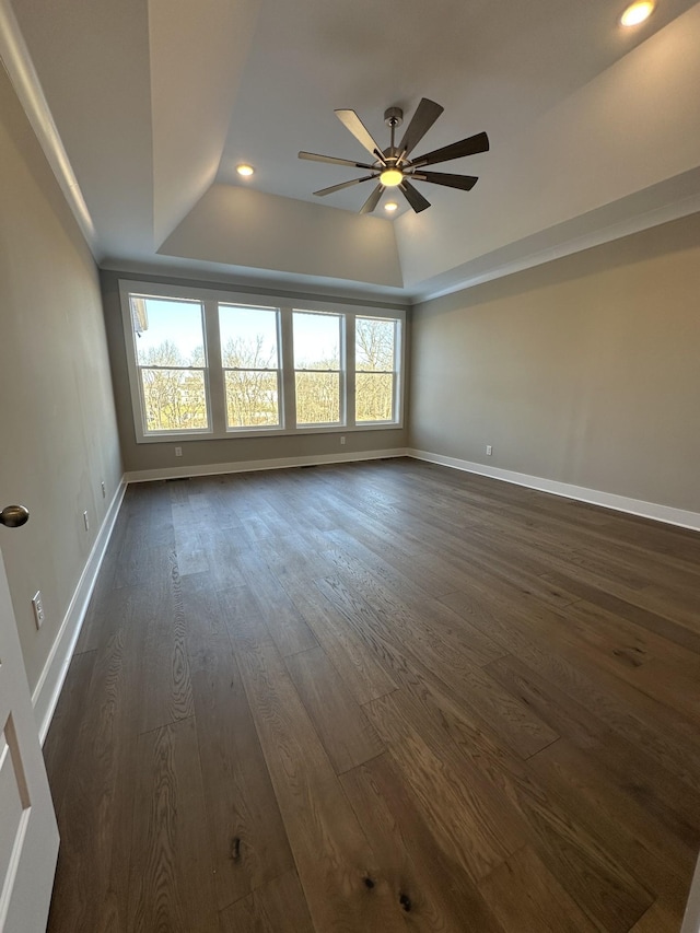 empty room featuring a raised ceiling, ceiling fan, a wealth of natural light, and dark hardwood / wood-style floors