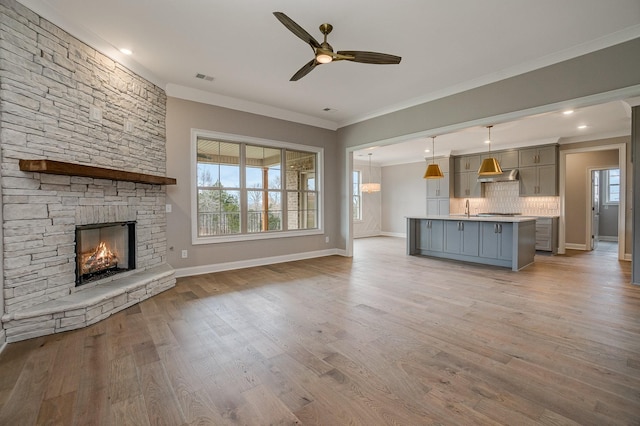 unfurnished living room featuring crown molding, a fireplace, ceiling fan, and light hardwood / wood-style floors