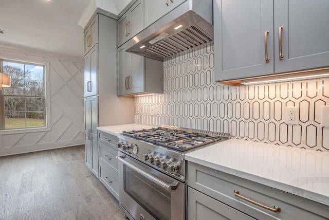 kitchen with gray cabinets, light stone countertops, light wood-type flooring, stainless steel range, and tasteful backsplash