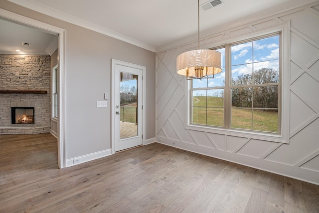 unfurnished dining area featuring a healthy amount of sunlight, a stone fireplace, crown molding, and light hardwood / wood-style flooring