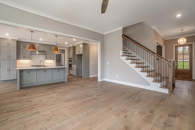 kitchen featuring decorative light fixtures, gray cabinets, an island with sink, and light hardwood / wood-style flooring