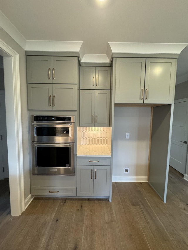 kitchen featuring stainless steel double oven, dark hardwood / wood-style floors, backsplash, crown molding, and gray cabinets