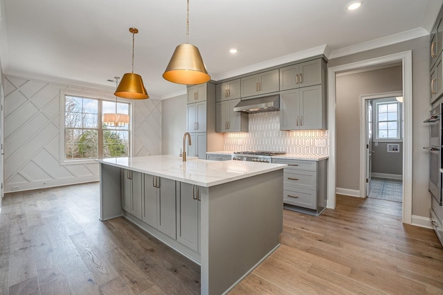 kitchen with hanging light fixtures, light stone counters, a wealth of natural light, and an island with sink