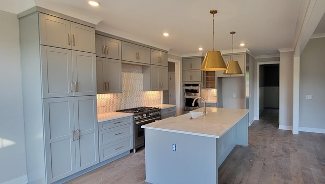 kitchen featuring light stone countertops, hanging light fixtures, stainless steel appliances, a center island with sink, and light wood-type flooring